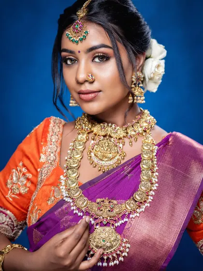 A stunning muhurtham look featuring a kasu mala (coin necklace) paired with a Lakshmi choker. The combination of purple and orange in her saree is beautifully complemented by the gold jewellery.