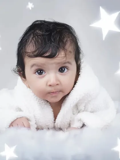A close-up of a newborn lying on a fluffy white cloud setup, surrounded by glowing stars. I focus on capturing their curious and innocent expressions in these themed shoots.