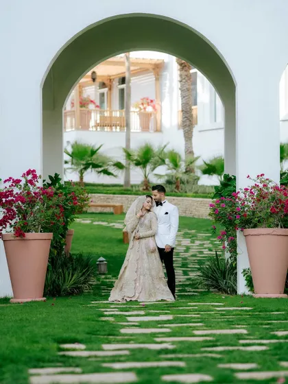A beautifully framed portrait of the couple in a garden with white arches, creating a sense of grandeur and romance.