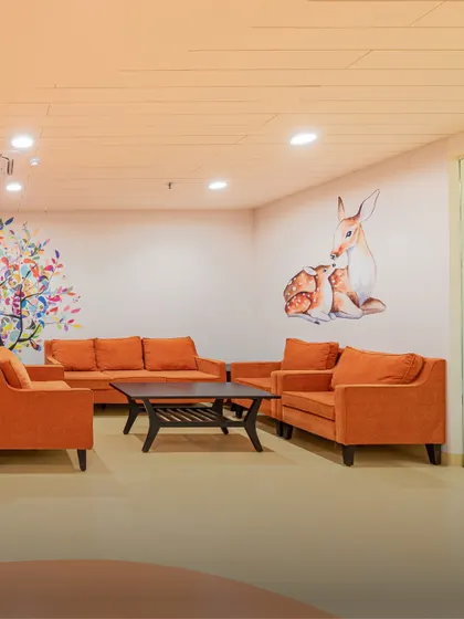 The same waiting area is shown with orange sofas, demonstrating how color can be used to create different moods. The consistent theme of nature and comfort provides a reassuring environment for families.