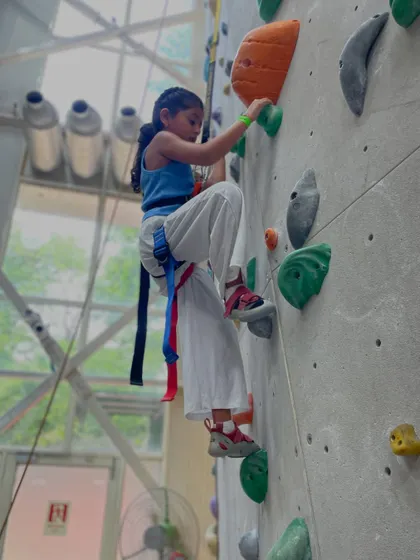 Dressed for success, a young girl reaches for her next hold. Climbing is a fantastic activity that builds full body strength and coordination in children.