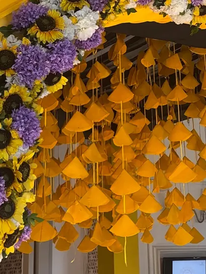 A unique and vibrant detail for a Haldi entrance. This close up shows the hanging yellow fabric cones and the lush arch of sunflowers and purple flowers that created a memorable entryway.