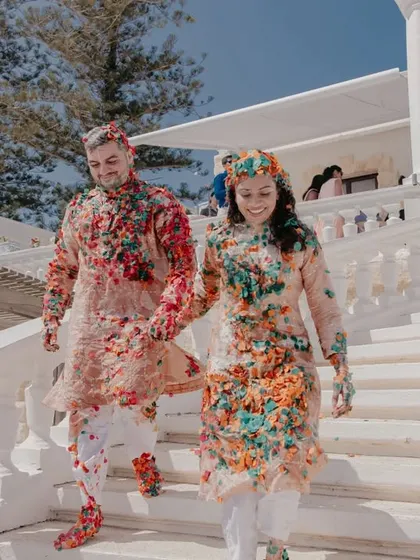 Hand in hand, the couple descends a grand white staircase, still covered in the remnants of their colorful and joyous haldi ceremony in Malta.