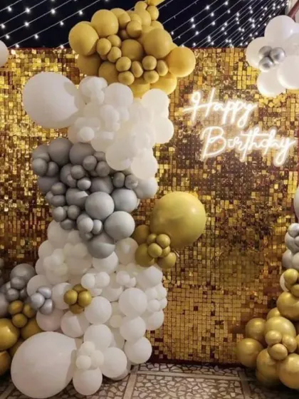 A fun and sparkly birthday backdrop with a gold sequin wall and a white, gold, and silver balloon garland. The 'Happy Birthday' neon sign adds the perfect finishing touch.