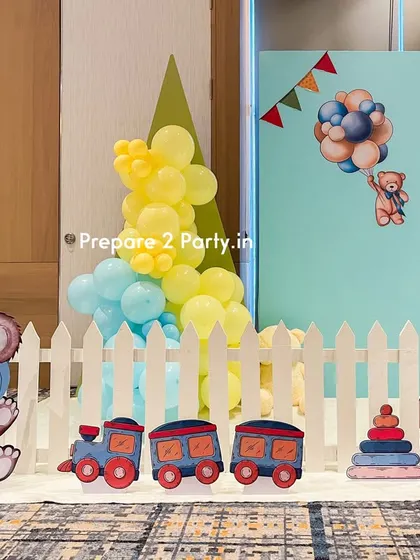 A detailed shot of the first birthday setup, focusing on the charming cutouts of teddy bears and a toy train placed in front of the white picket fence.