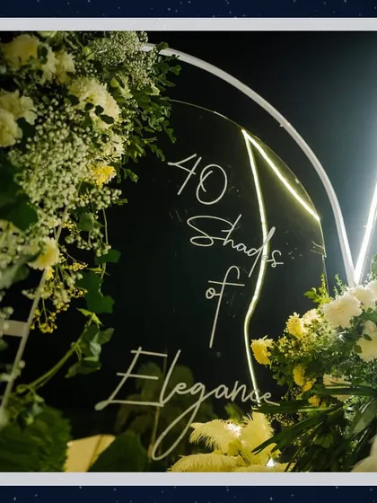 The theme of an event should be woven into every detail. This custom acrylic sign, reading '40 Shades of Elegance' and framed with beautiful white florals and soft lighting, served as a chic focal point.