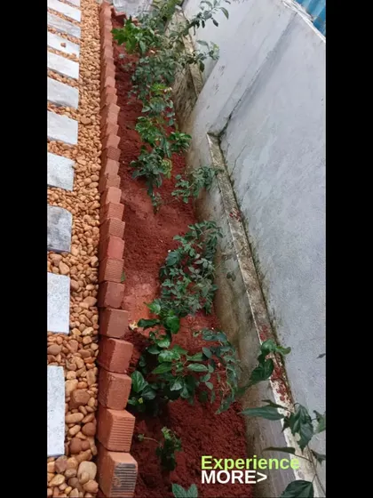 This garden bed combines a red soil planting area with a stone and pebble pathway, separated by a brick border.