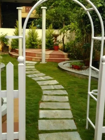 A classic English garden aesthetic with a white picket fence and archway leading to a curved stone path. This design creates a charming and whimsical entrance.