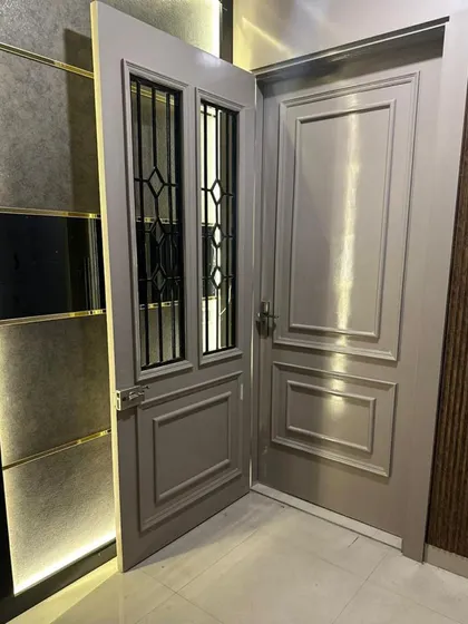 A custom-designed main door with a sophisticated grey finish. The door features classic paneling and two glass inserts with a geometric grill design, creating an elegant and secure entryway.