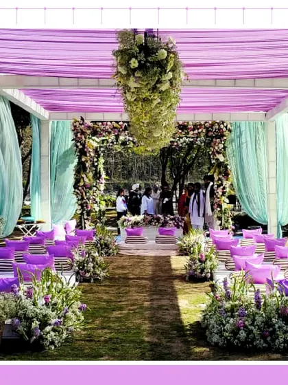 A stunning aisle view of a destination wedding in Jim Corbett, with purple and sea-green drapes and a ceiling of hanging flowers.
