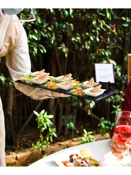 A server presenting a tray of appetizers to a guest enjoying a glass of rosé, capturing a moment of relaxed, sophisticated hospitality.
