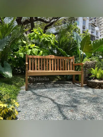 A classic wooden park bench sits on a gravel clearing, surrounded by a dense thicket of tropical plants. This simple touch creates an inviting destination within the garden, encouraging moments of pause.