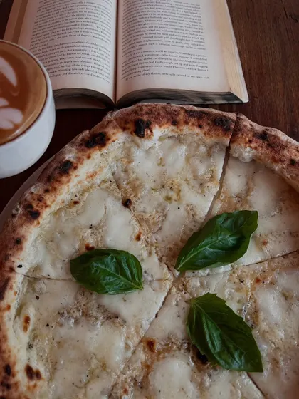 A quiet moment with a book, coffee, and our Pizza Bianca. This is the Leo's vibe.