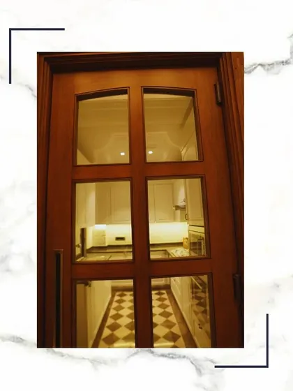 A glimpse through this classic glass-paneled wooden door reveals a stunning kitchen, showcasing how we design spaces that are connected yet distinct.