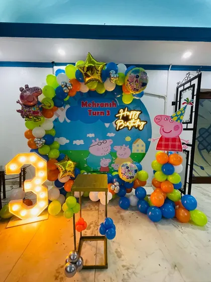 A Peppa Pig party with a custom printed backdrop. The scene is framed by a multi-colored balloon arch and includes a large light-up '3' and character cutouts.
