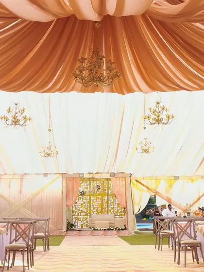 An elegant tented setup for a day wedding at Wood Castle, Jim Corbett, with soft peach drapes and crystal chandeliers.