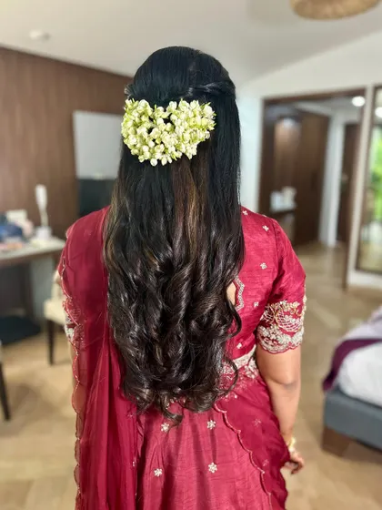 A half-up hairstyle with beautiful curls, adorned with a string of fresh jasmine (gajra) for a traditional yet modern feel.