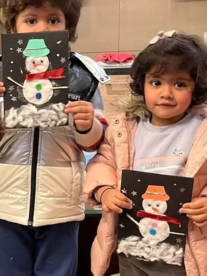 Two of our youngest artists hold up their finished snowman cards. These mixed-media projects are great for teaching toddlers about different textures and materials.