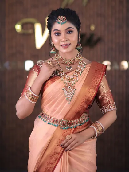 A full set from a photoshoot featuring a lovely peach-colored silk saree. The drape is kept simple and elegant to highlight the beautiful color and the intricate temple jewellery.