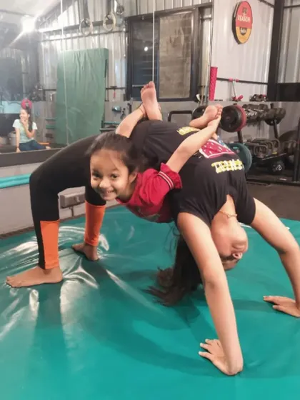 This is a playful two-person pose where one student holds a backbend while the other balances on top. It’s a fun drill we use to improve flexibility and partner coordination.