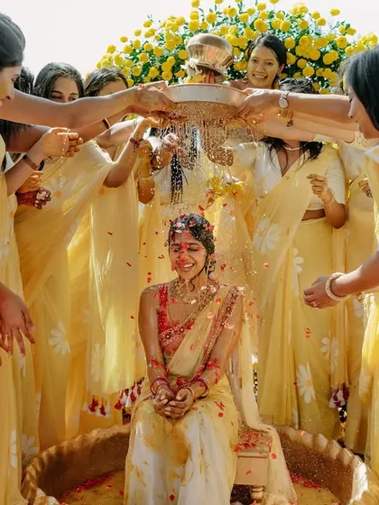 A joyous moment from a Haldi ceremony, with the bride being showered with petals by her bridesmaids in front of a beautiful floral backdrop.