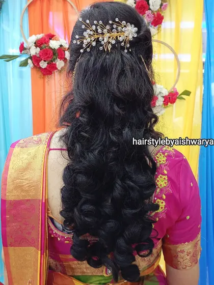 A classic half-up hairstyle with soft, bouncy curls at the ends. The look is finished with a sparkling hair accessory, perfect for an evening function.