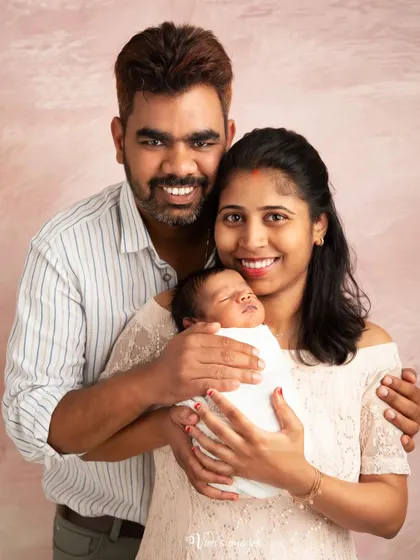 A classic first family portrait. This image showcases the happy new parents with their sleeping newborn, a timeless keepsake to announce their little one to the world.