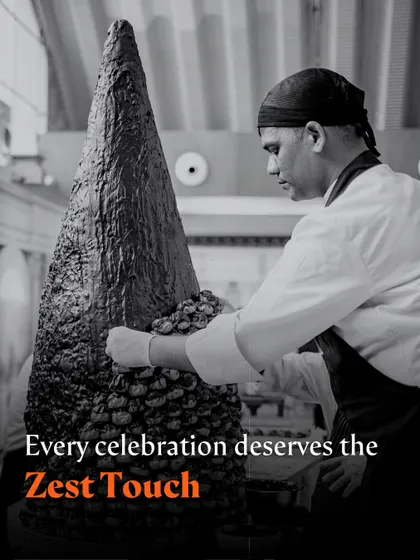 A black and white photo of a chef meticulously assembling a large dessert tower.