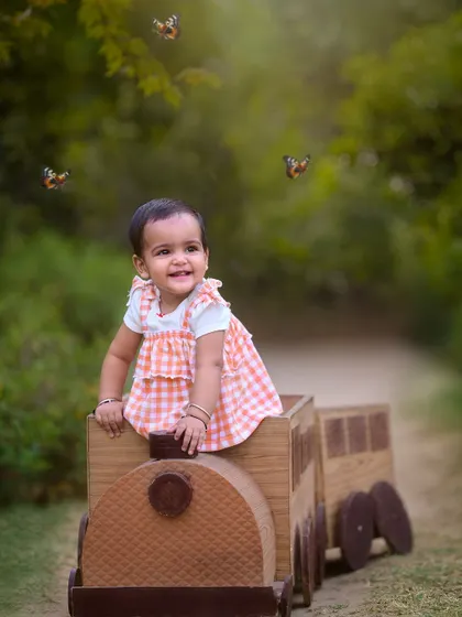 A happy journey into her next year. This little girl enjoys a ride in a wooden train prop, surrounded by magical butterflies in a beautiful outdoor setting for her first birthday shoot.