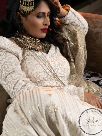 A high-fashion, avant-garde look from an editorial shoot. The makeup is bold and confident, with a deep red lip and smokey eyes, paired with layered, modern jewellery and an all-white outfit.
