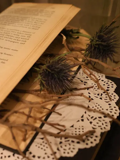 An intimate close-up of dried thistles and twigs placed inside an open book. This highlights our focus on creating unique, small-scale visual moments within a larger event design.