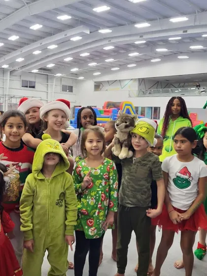 A group of happy kids in their festive holiday sweaters, Grinch onesies, and Santa hats, posing for a photo during our Grinchmas Friday Fun Night.