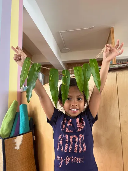A child joyfully holds up a completed leaf toran. This simple, nature-based craft is a beautiful decoration and a source of great pride for the creator.