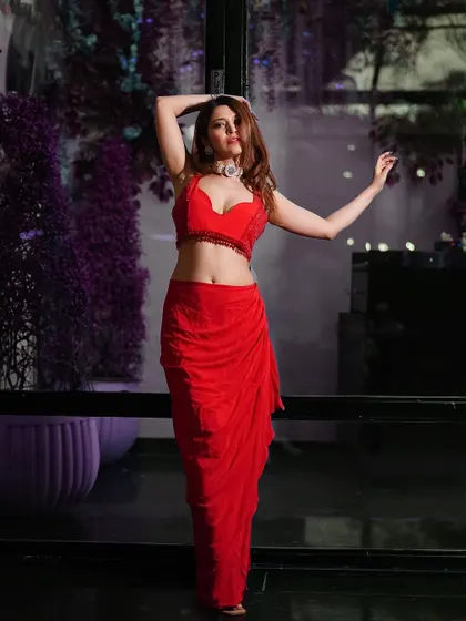 A full-length pose that shows off the unique silhouette of the draped red saree. The pose is strong and confident, perfect for a fashion-forward brand.