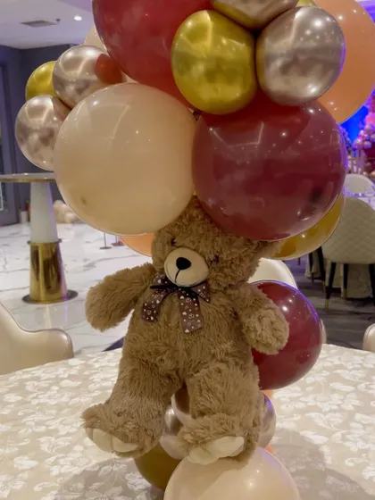 A close-up of a teddy bear table centerpiece, using a rich palette of burgundy, peach, and gold balloons.