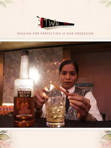 A female bartender expertly smokes a cinnamon stick to garnish a cocktail, adding a warm, spicy aroma to the drink.