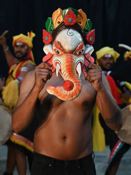 A Ganesha mask from Nepal, held by a Dollu Kunitha dancer from Karnataka. This image captures a beautiful fusion of cultures, celebrating the protective power of these mythical beings.