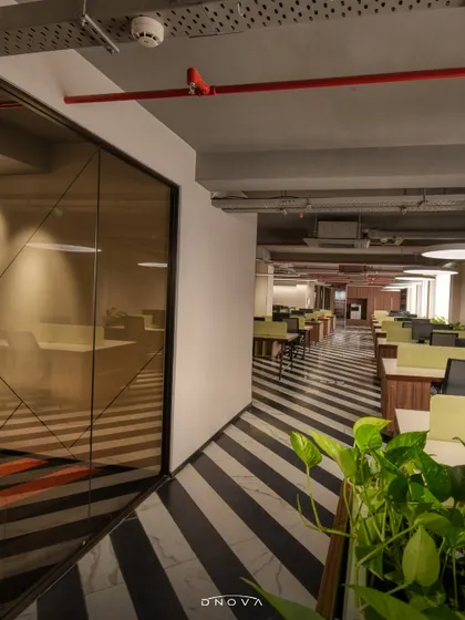 The bold black-and-white striped flooring at the Lohia Designco office creates a strong visual pathway through the workspace. This general contracting project included integrating biophilic elements like planters to soften the modern design.