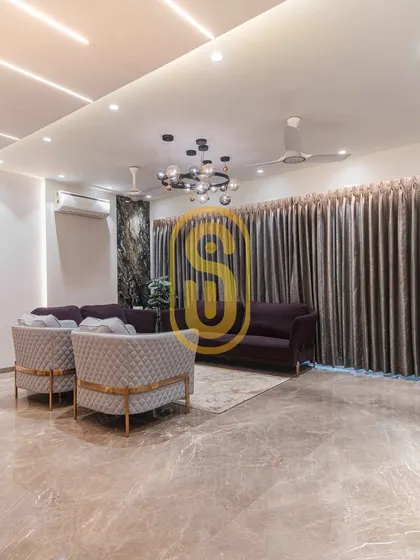 A wide-angle view of the living room, emphasizing the expansive marble flooring and the sophisticated lighting design. The combination of a central chandelier and linear ceiling lights provides layered illumination.