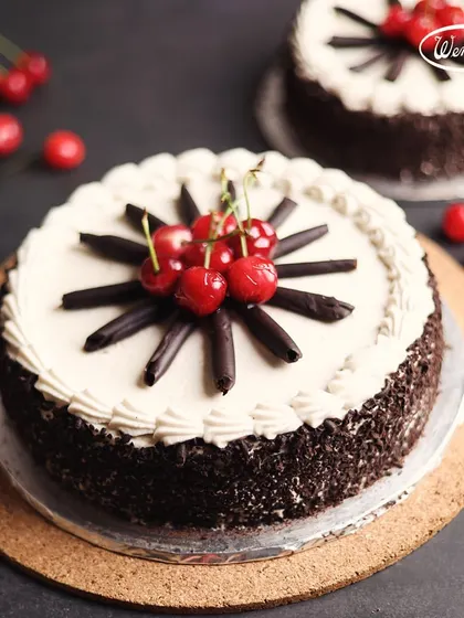 This is our classic Black Forest Cake, a crowd pleaser for generations. We layer soft chocolate sponge with fresh cream and cherries, cover it in more cream and chocolate shavings, and top it with a fan of chocolate sticks and bright red cherries.