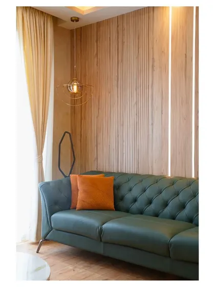 A still from a recent project, this living room corner features a tufted green leather sofa against a fluted wood wall, with a modern pendant light adding a touch of industrial chic.
