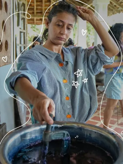 A guest carefully dips her bound fabric into a pot of rich, natural indigo dye. This is the moment of transformation, where the cloth begins to absorb the color that will bring the pattern to life.