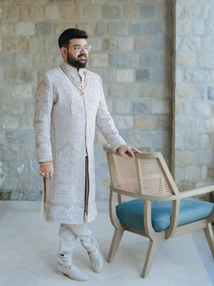 A classic portrait of the groom in his elegant ivory sherwani, standing with a poised and confident look.