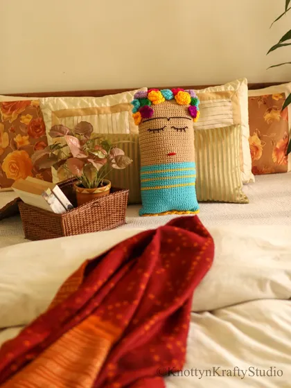 The Frida cushion, styled in a bedroom setting with a warm red throw and a basket of books. It shows how a single piece can tie a whole look together.