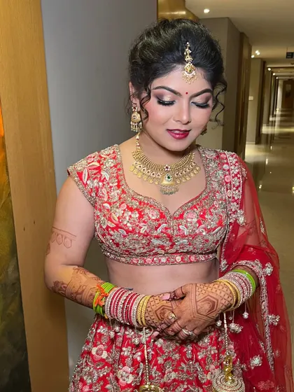 A beautiful bridal portrait in a classic red lehenga. The makeup features a soft smokey eye with a hint of shimmer and a bold red lip, creating a timeless and elegant look.