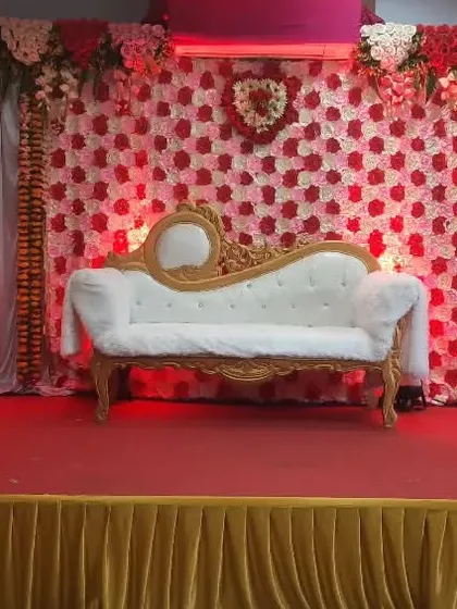 A beautiful engagement stage featuring a red and white rose wall backdrop. The classic white divan sofa and focused spotlights make this a perfect spot for the couple's photos.