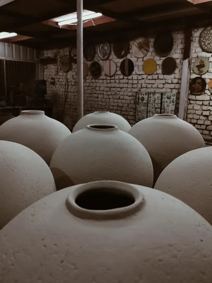 A group of bisque-fired moon jars, their forms creating a landscape of curves in the studio. The play of light and shadow on the raw clay highlights their shape before the glaze is applied.