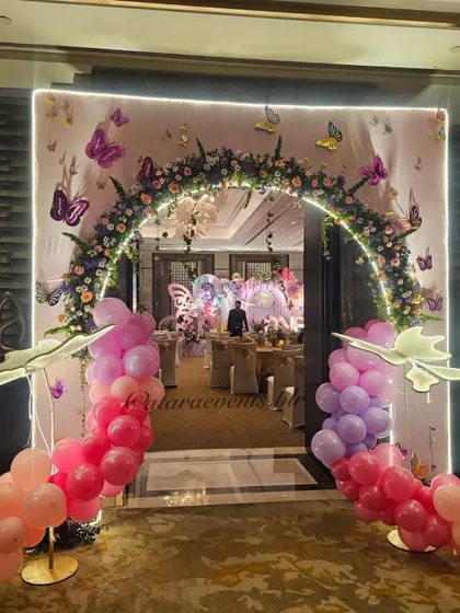 A stunning floral and balloon archway creating a grand entrance for a butterfly-themed birthday. The lit arch and butterfly-adorned backdrop promise a magical experience inside.
