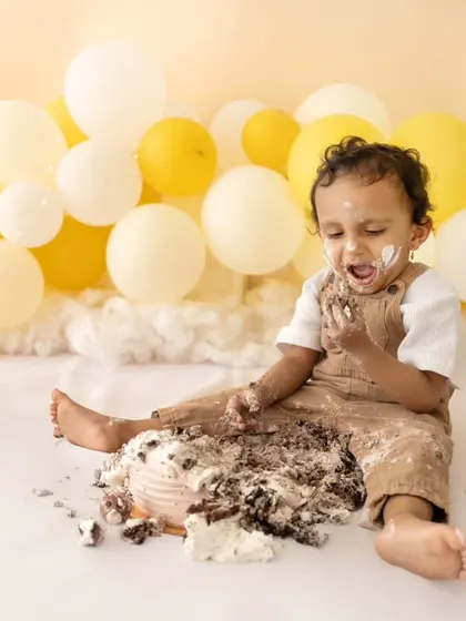 This little guy is loving his cake smash! The yellow and white balloon backdrop adds a cheerful and bright touch to the celebration.