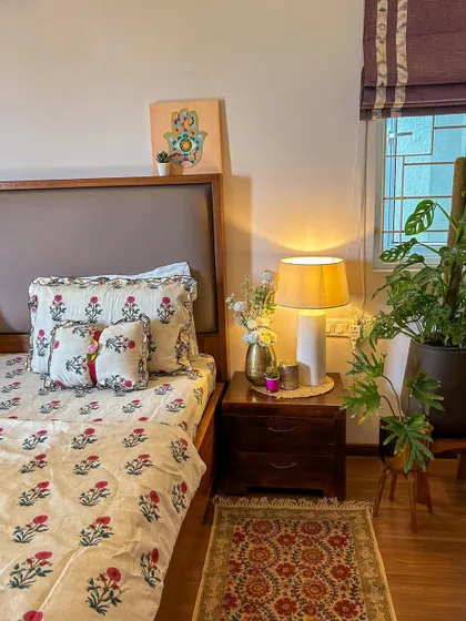 A close-up of the bedside table, styled with a simple lamp, a vase of flowers, and a small plant.